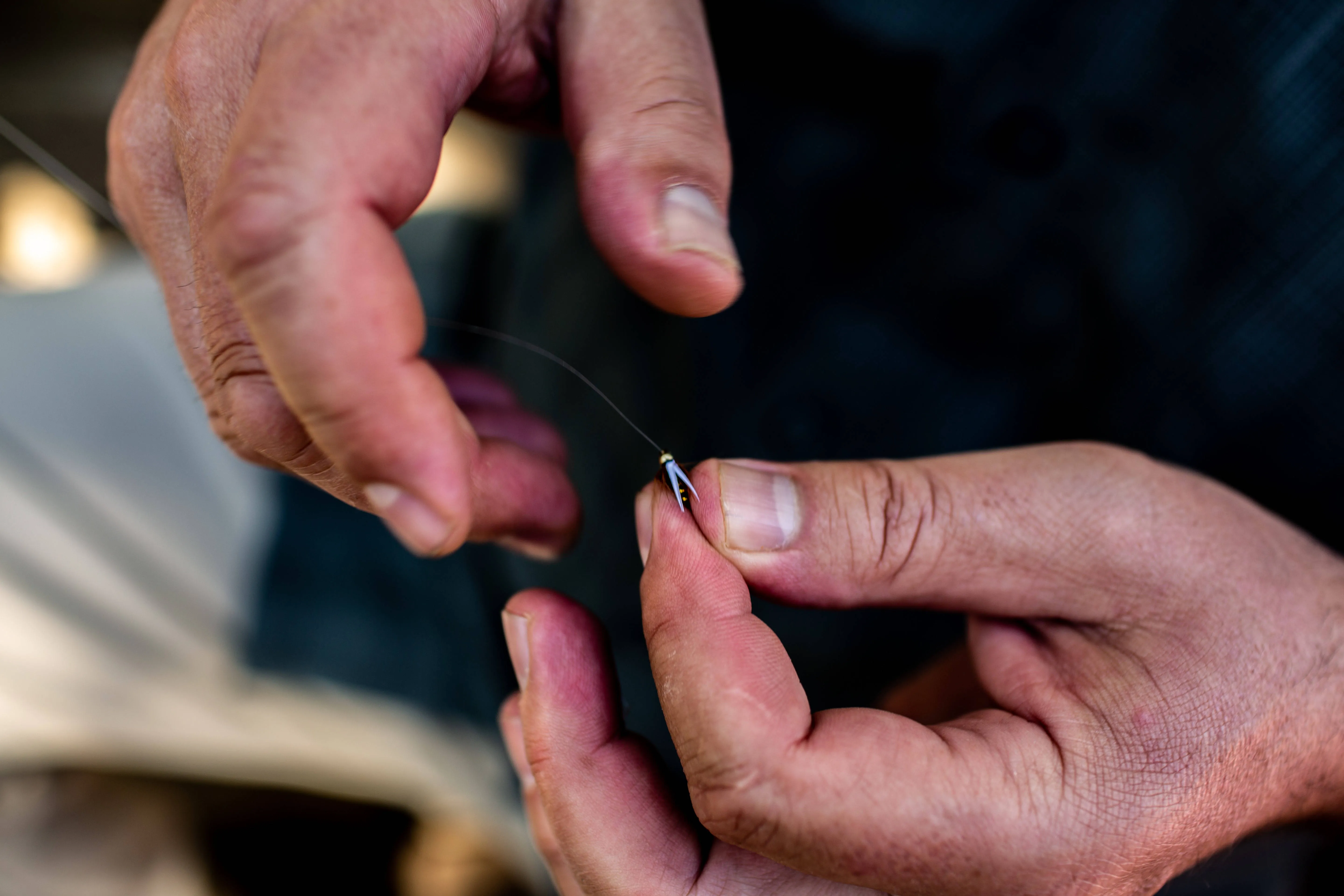 Hands tying a small fly onto tippet
